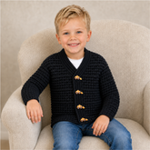 Boy in blue jeans wears a black Aaron V-neck crochet cardigan on a cream chair. Digital pattern PDF, sizes 3 to 10 Years.