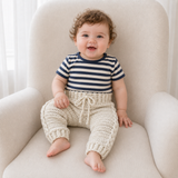 Boy in a gray and cream T-shirt wears cream Cooper cable-detail crochet pants on a cream chair. Digital pattern PDF, NB–2Y.