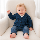 Baby in blue jeans wears a blue Devon V-neck crochet cardigan on a cream chair. Digital pattern PDF, sizes 0 to 2 Years.