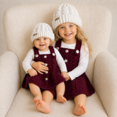 Older girl and baby on a cream chair wear maroon Harper cabled crochet dresses and white Ethan hats. Digital pattern PDF.