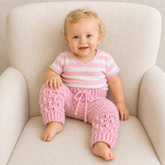 Baby wears pink Izzy crochet pants with a pink-and-white striped T-shirt on a cream chair; digital pattern PDF.