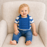 Toddler wears blue Jacob crochet bib over blue-and-white striped shirt with blue jeans on a cream chair. Digital pattern PDF.