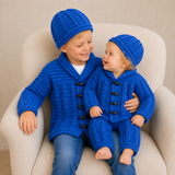 Older boy and baby wear blue Jacob crochet cardigan and hat; baby wears matching pants on cream chair. Digital pattern PDF