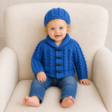 Baby wears blue Jacob crochet cardigan and hat with blue jeans on a cream chair. Digital pattern PDF.