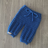 Jacob crochet baby pants with Jacob's Ladder stitch laid diagonally on wood. Digital pattern PDF, Newborn to 2 Years.