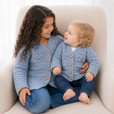 Older girl and baby in jeans wear Kasey crochet cardigans on a cream chair. Digital pattern PDF, sizes Newborn to 10 Years.