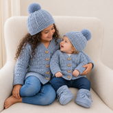 Girl and baby in jeans sit on cream chair wearing Kasey crochet cardigans and hats; baby wears booties. Digital pattern PDF.