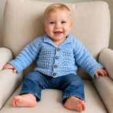 Baby in blue jeans wears a blue Luke crochet cardigan on a cream chair. Digital pattern PDF, size 0 to 3 Months.