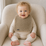 Baby in a white and gold striped onesie wears a gold Renee crochet bib on a cream chair. Digital pattern PDF.