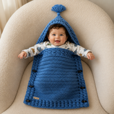 Baby lying in the River blue cabled crochet cocoon with arms out and wooden side toggles for a digital pattern PDF.