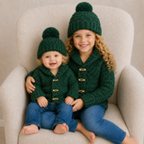 Older girl and baby wear green Rocky shawl-collar crochet sweaters and hats on a cream chair. Digital pattern PDF, NB–10Y.
