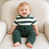 Baby in a green and white striped T-shirt wears green Rocky crochet pants on a cream chair. Digital pattern PDF, NB–2Y.