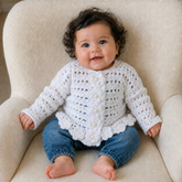 Baby in blue jeans wears a Shannyn crochet cardigan on a cream chair. Digital pattern PDF, size 0 to 3 Months.