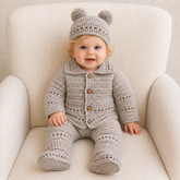 Baby in Zac light-grey crochet cardigan, pants, booties and double-pompom hat on a cream chair for digital pattern PDFs.