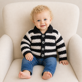 Baby in blue jeans wears a black and silver striped Ziggy crochet collared cardigan on a cream chair. Digital pattern PDF