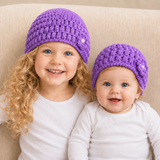 Older girl and baby on a cream chair wear purple Beth puff-stitch crochet beanies. Digital pattern PDF, Preemie–10Y.