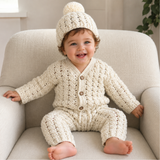 Baby on a cream chair wearing cream Caleb crochet cable-detail cardigan, pom-pom hat and pants. Digital pattern PDF set