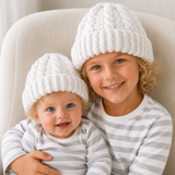 Older child and baby on cream chair wear white Ethan cabled crochet hats. Digital pattern PDF, sizes Preemie to 10 Years.