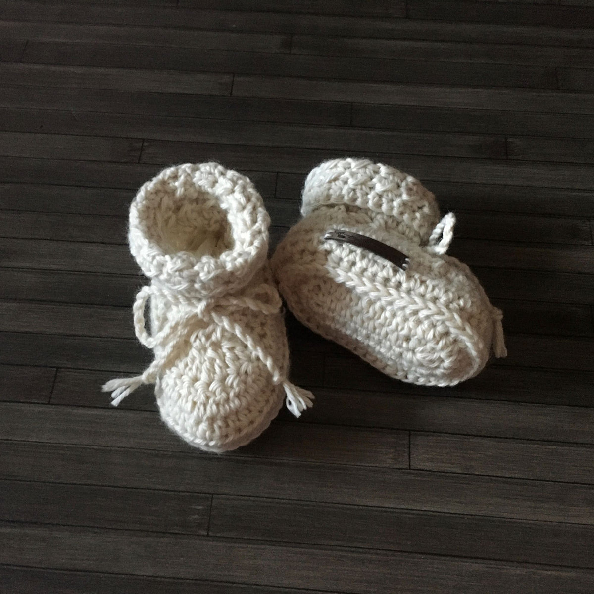 Cream Grayson crochet baby booties on wood, one upright and one lying down. Digital pattern PDF, sizes Preemie to 1 Year.