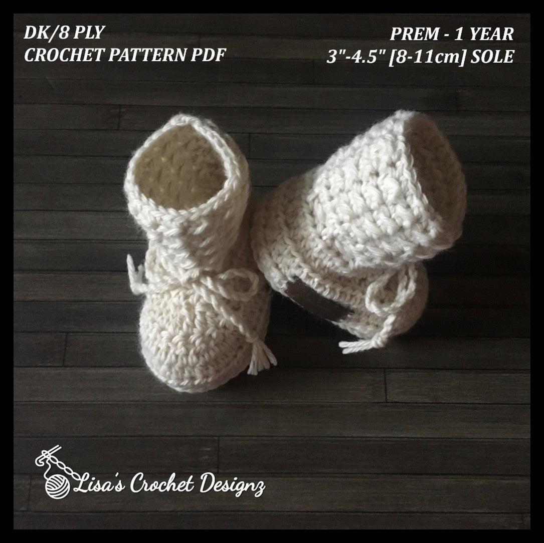 Cream Grayson crochet baby booties standing on wood, one leaning against the other. Digital pattern PDF details, Preemie–1Y.
