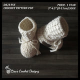 Cream Grayson crochet baby booties standing on wood, one leaning against the other. Digital pattern PDF details, Preemie–1Y.