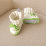 Ivy white, gray and green cuffed crochet booties on cream chair, one upright and one lying down. Digital pattern PDF, NB–12M.