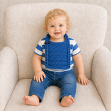 Toddler wears blue Jacob crochet bib over blue-and-white striped shirt with blue jeans on a cream chair. Digital pattern PDF.