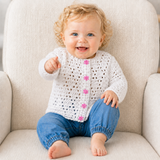 Baby in blue jeans on a cream chair points while wearing a white Rihanna crochet cardigan. Digital pattern PDF, 0–3M.