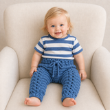 River blue cabled crochet baby joggers worn by a baby on a cream chair for a newborn-to-2-years digital pattern PDF.