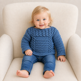River blue cabled crochet sweater worn by a smiling baby boy on a cream chair for a 0–3M-to-12Y digital pattern PDF.