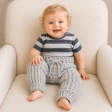 Baby on a cream chair wearing gray Theo crochet pants in Aran 10 Ply yarn. Digital pattern PDF, sizes Newborn to 2 Years.