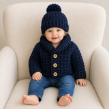 Baby wearing William navy crochet shawl-collar cardigan with wooden buttons and pompom hat for a digital pattern PDF.