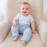 Baby in a white T-shirt wears pale blue Zeb crochet pants on a cream chair. Digital pattern PDF, sizes Newborn to 2 Years.